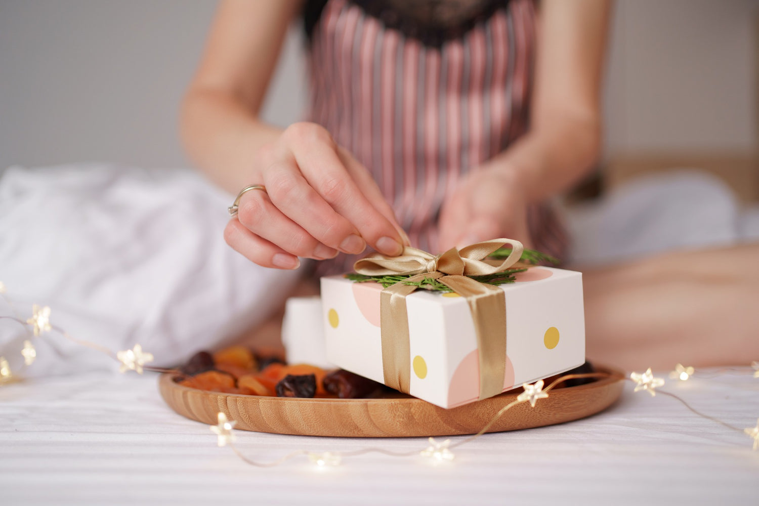 woman-hand-unwrapping-gift-while-sitting-bed-with-lights-white-sheets.jpg__PID:f8753e52-27d2-4e71-a482-d79588b2e369